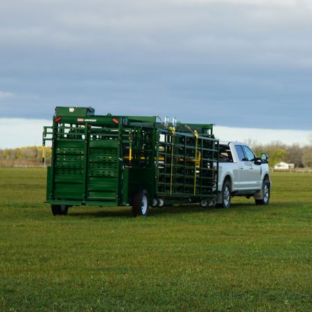 A white truck towing the portable corral system through a pasture